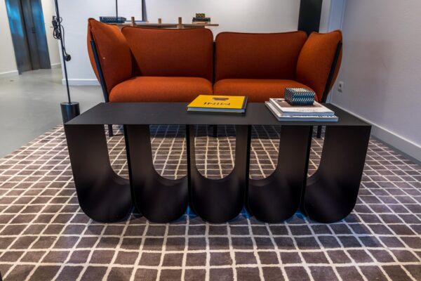 Moderne zithoek met een oranje bank, zwart designer salontafel en boeken op een geruit vloerkleed.